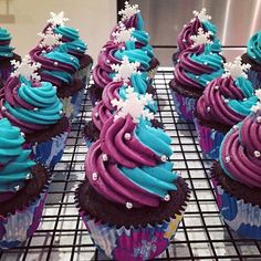 cupcakes with blue and purple frosting on a cooling rack in a kitchen