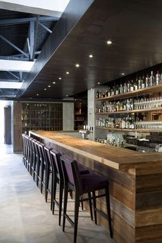 an empty bar with many bottles on the shelves and stools in front of it