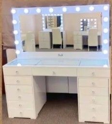 a white vanity with lights on it in front of a mirror that is reflecting the room