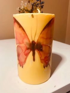 a candle with a butterfly on it sitting on a table next to a potted plant