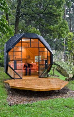 a small cabin in the middle of a forest with two people standing inside and looking at it