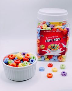 a bowl filled with fruit loops next to a container of cereals on a white surface