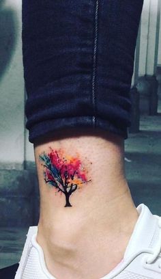 a woman's ankle with a colorful tree tattoo on her left side ribcage