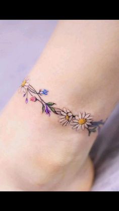 a woman's foot with daisies and leaves tattoo on the side of her leg