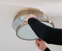 a person is adjusting the light on a ceiling fixture in a room with white walls