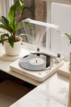 a record player sitting on top of a table next to a potted plant in front of a window