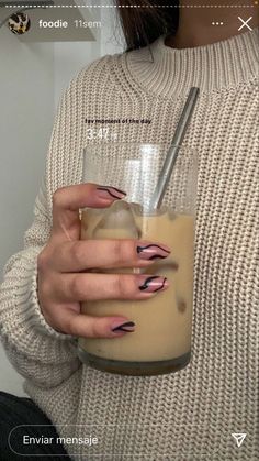 a woman holding a drink in her right hand with pink and black nail designs on it