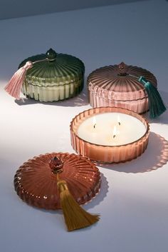 three candles sitting next to each other on top of a white tablecloth with tassels