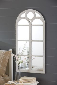 a white table topped with a vase filled with flowers next to a mirror and window