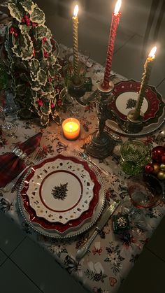 the table is set for christmas dinner with candles and plates on it, along with other holiday decorations