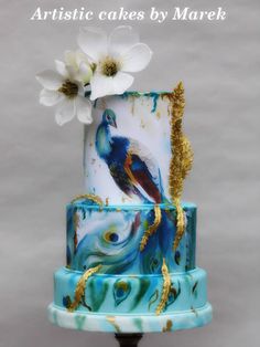 a three tiered cake decorated with peacocks and flowers on a metal stand in front of a gray background