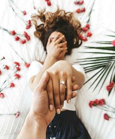 a man and woman holding hands while laying on a bed with red flowers in the background