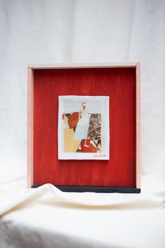 a wooden frame with a painting in it on a white sheeted surface next to a cloth