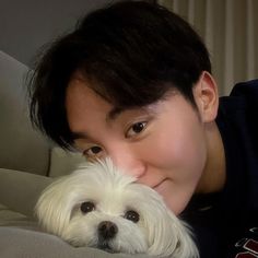 a man holding a white dog on top of a couch in front of his face