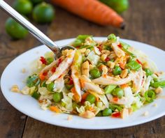 a white plate topped with salad next to carrots and celery on top of a wooden table