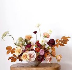 a vase filled with lots of flowers sitting on top of a wooden table next to a white wall