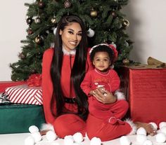 a woman sitting next to a baby in front of a christmas tree