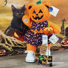 an orange teddy bear dressed up as a pumpkin with a black cat behind it and halloween decorations