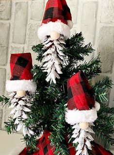 a christmas tree with red and white plaid hats on it's head, sitting in front of a brick wall that says adorable pine cone christmas gnomes