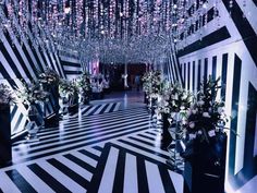 a black and white striped room with chandeliers hanging from the ceiling, flowers in vases on the floor