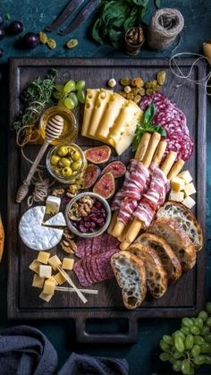 an assortment of cheeses and meats on a cutting board with breadsticks