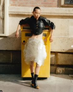 a woman standing in front of a yellow machine with feathers on it's skirt