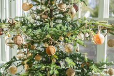 a christmas tree with ornaments hanging from it's branches in front of a window