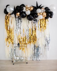 balloons and streamers are hanging on the wall in front of a gold and black backdrop