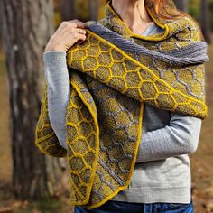 a woman wearing a yellow and gray knitted shawl in front of some trees