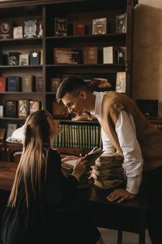 a man and woman sitting at a table in front of a book shelf with books on it