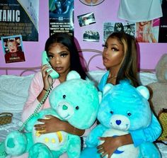 two women sitting on a bed holding teddy bears while one talks on the cell phone