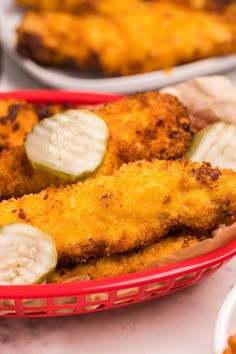 fried fish fillets in a red basket with pickles and sauces on the side