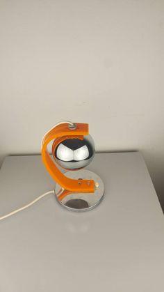 an orange and silver object sitting on top of a white table next to a gray wall