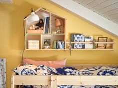 a bed with blue and white pillows in front of a shelf filled with books on top of it