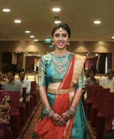 a woman in a blue and orange sari standing next to red chairs with people watching