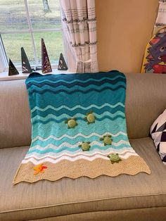 a crocheted blanket sitting on top of a couch in front of a window