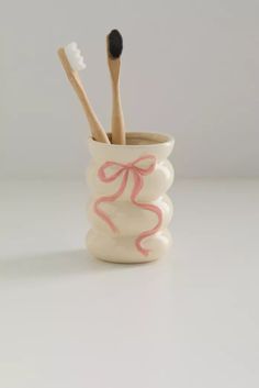 two toothbrushes in a cup with pink bows