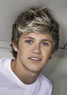 a young man with blonde hair wearing a white t - shirt and looking at the camera