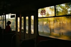 a person sitting on a bus looking out the window at trees and buildings in the distance