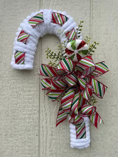 a red, white and green christmas wreath hanging on the side of a building with ribbon