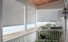 an empty balcony overlooking the beach and ocean with blinds on the windows looking out onto the water