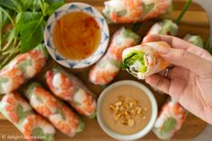 a person holding a piece of food in front of some vegetables and dipping sauces