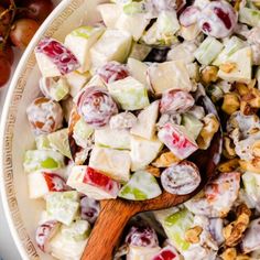 a salad with grapes, nuts and dressing in a bowl next to a wooden spoon