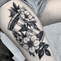 a woman's thigh with flowers and an hourglass tattoo