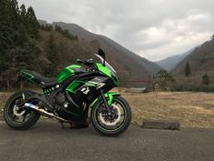 a green and black motorcycle parked on the side of a road in front of mountains