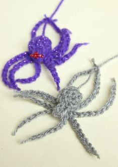 there are two crocheted spiders on the white table together, one purple and one gray