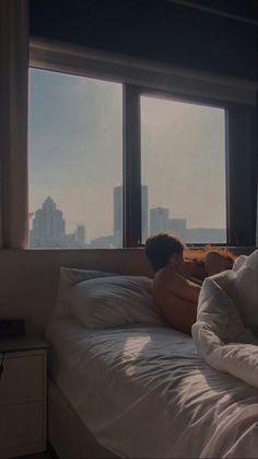 a man laying on top of a bed in front of a window next to a night stand