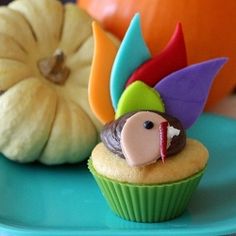 a cupcake decorated like a turkey sitting on a plate next to some pumpkins