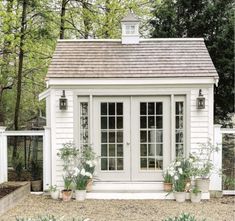 a small white shed with potted plants in front