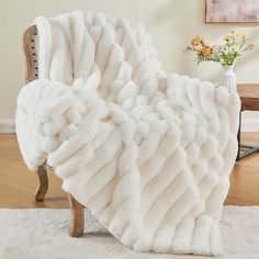 a white blanket sitting on top of a wooden chair next to a vase with flowers